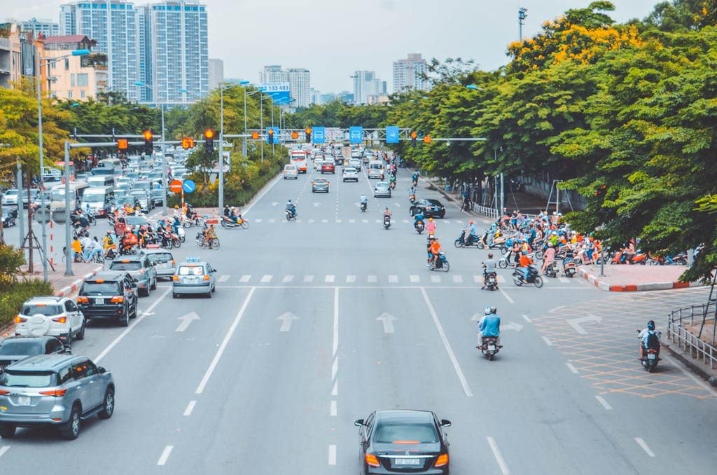 A bustling city intersection with cars and motorbikes at a stoplight during the day.