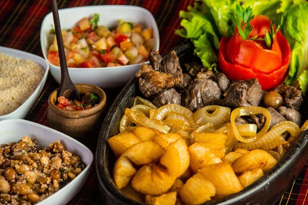 A delicious spread of traditional Brazilian dishes featuring beef, plantains, and vibrant salads.