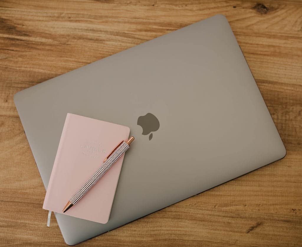 A sleek workspace featuring a laptop, pink notebook, and pen on a wooden desk.