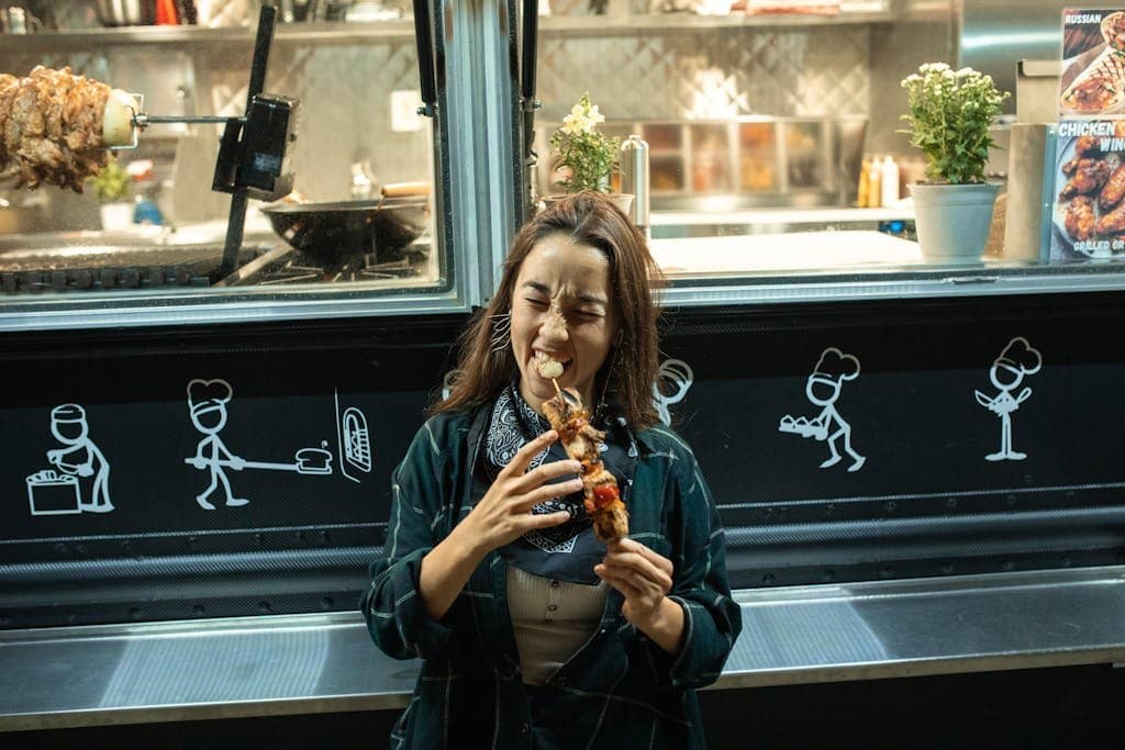 Smiling woman biting into a delicious kebab at a vibrant street food truck.