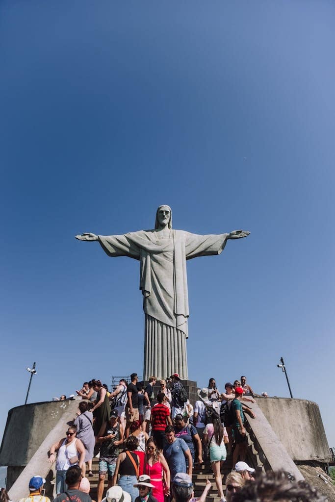 Tourists visit Christ the Redeemer in Rio de Janeiro under a clear blue sky.