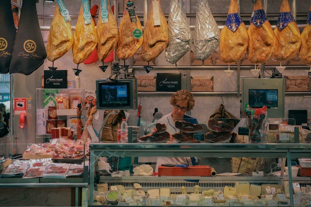A bustling market stall in Valencia, Spain, showcasing jamón and various cheeses.