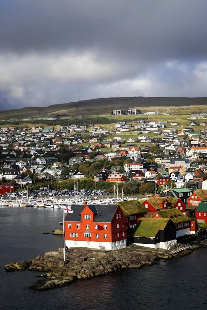 Picturesque coastal village in Faroe Islands showcasing traditional red and turf-roofed houses, embraced by serene landscape.