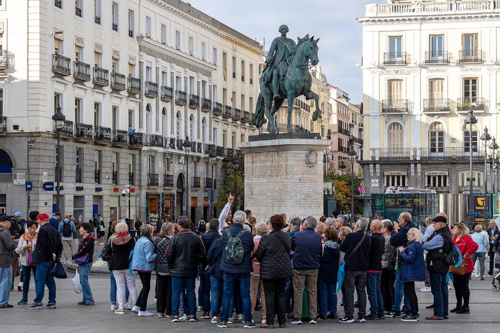 Tourists gather around the equestrian statue in Madrid's Puerta del Sol. Vibrant urban scene.
